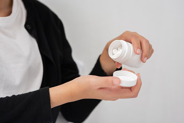 Uma mulher colocando em suas mãos pílulas brancas que estão dentro de um pote