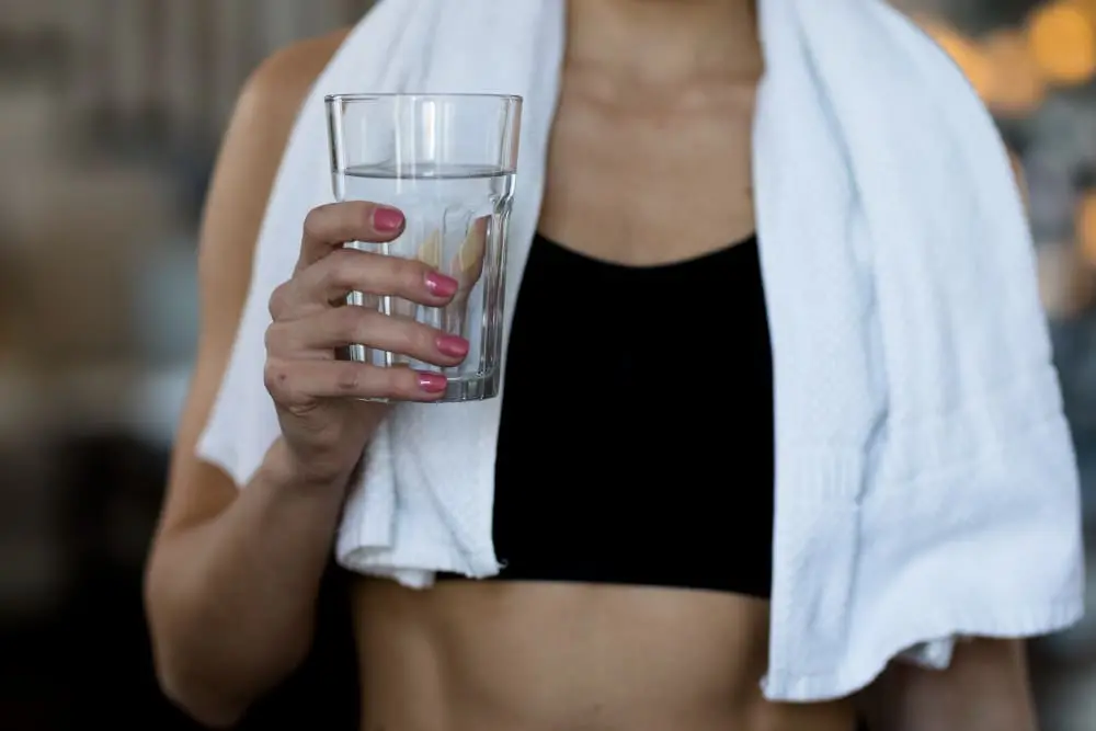 mulher-branca-usando-top-esportivo-preto-com-uma-toalha-nos-ombros-segurando-um-copo-de-agua